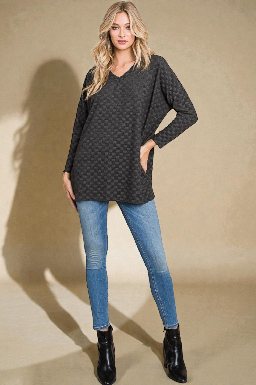 Woman wearing a dark patterned sweater, blue jeans, and black boots on a beige background