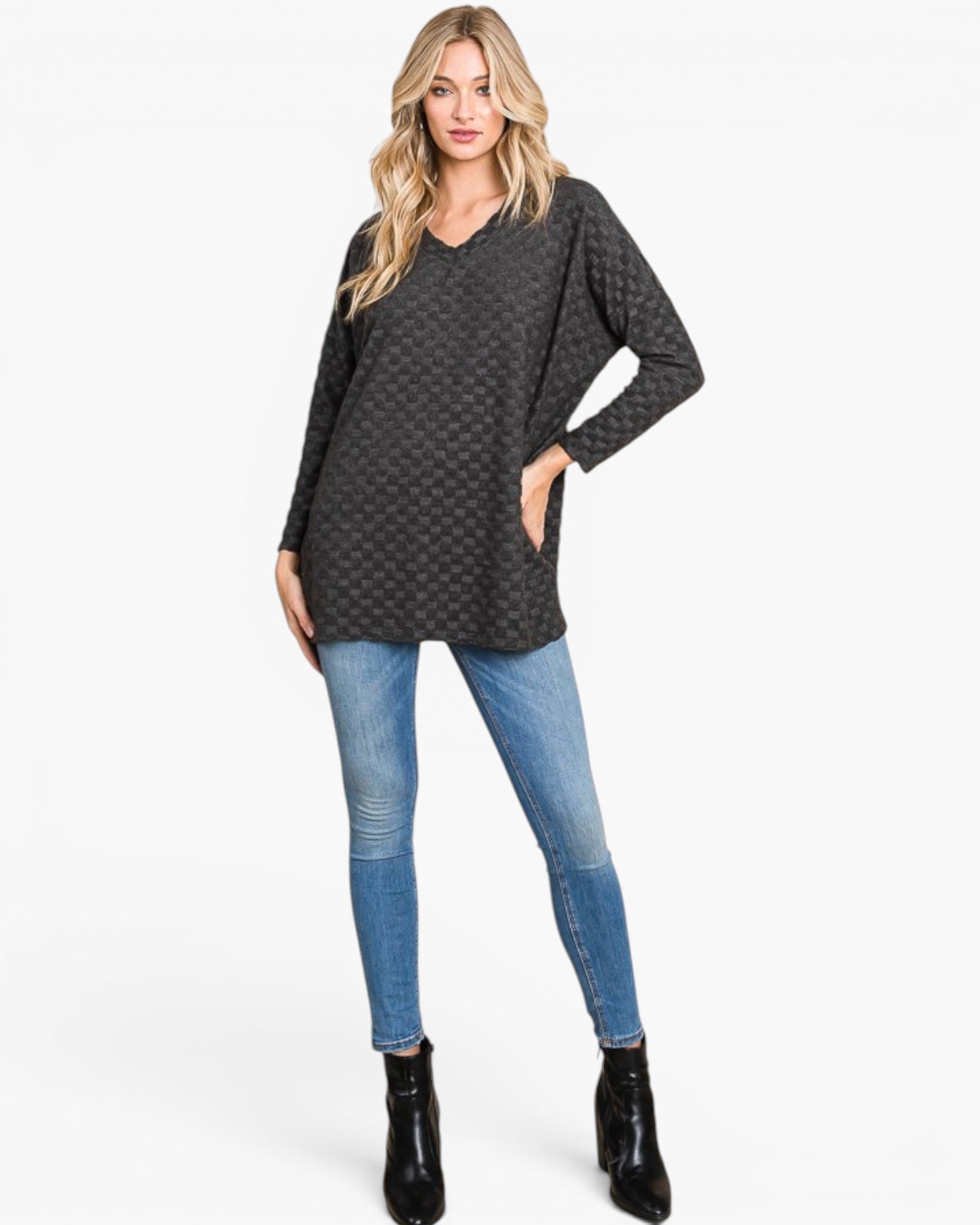 A woman modeling a dark gray long-sleeve tunic top with a subtle geometric pattern, paired with blue skinny jeans and black ankle boots, against a plain white studio background.