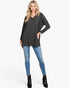 A woman modeling a dark gray long-sleeve tunic top with a subtle geometric pattern, paired with blue skinny jeans and black ankle boots, against a plain white studio background.