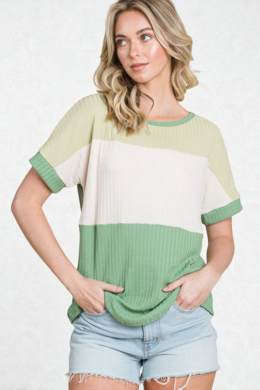 Woman wearing a green and white color-blocked top with denim shorts on a white background