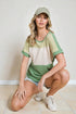Woman wearing a green and beige outfit with a cap, sitting on the floor.