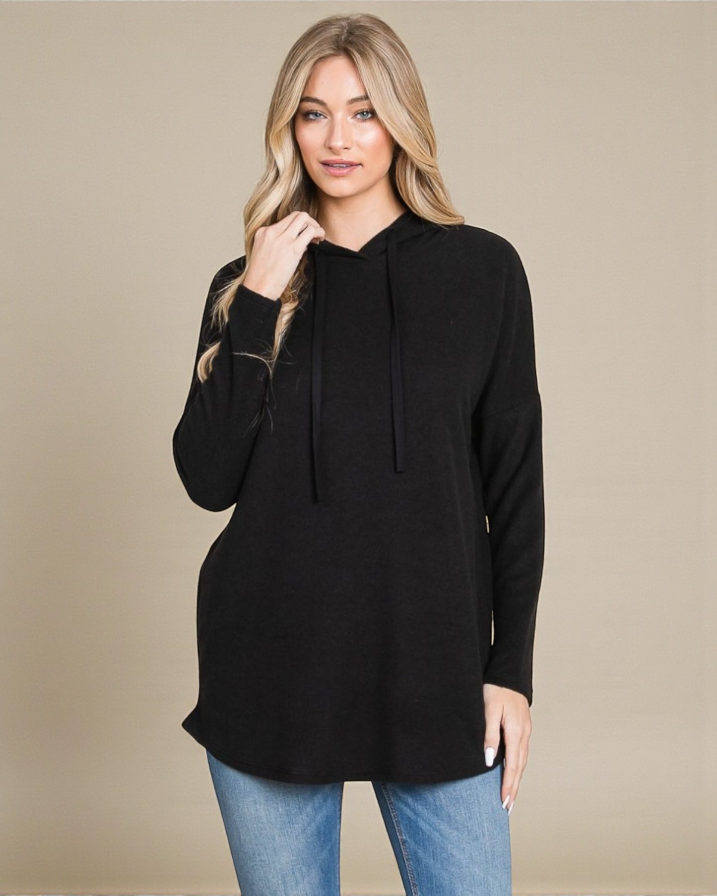 Woman wearing a black hoodie and blue jeans against a beige background