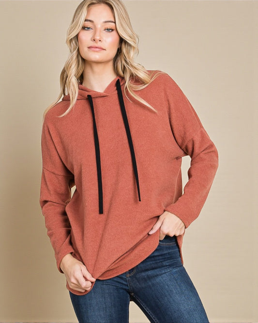 Woman wearing a rust-colored hoodie with black drawstrings on a beige background