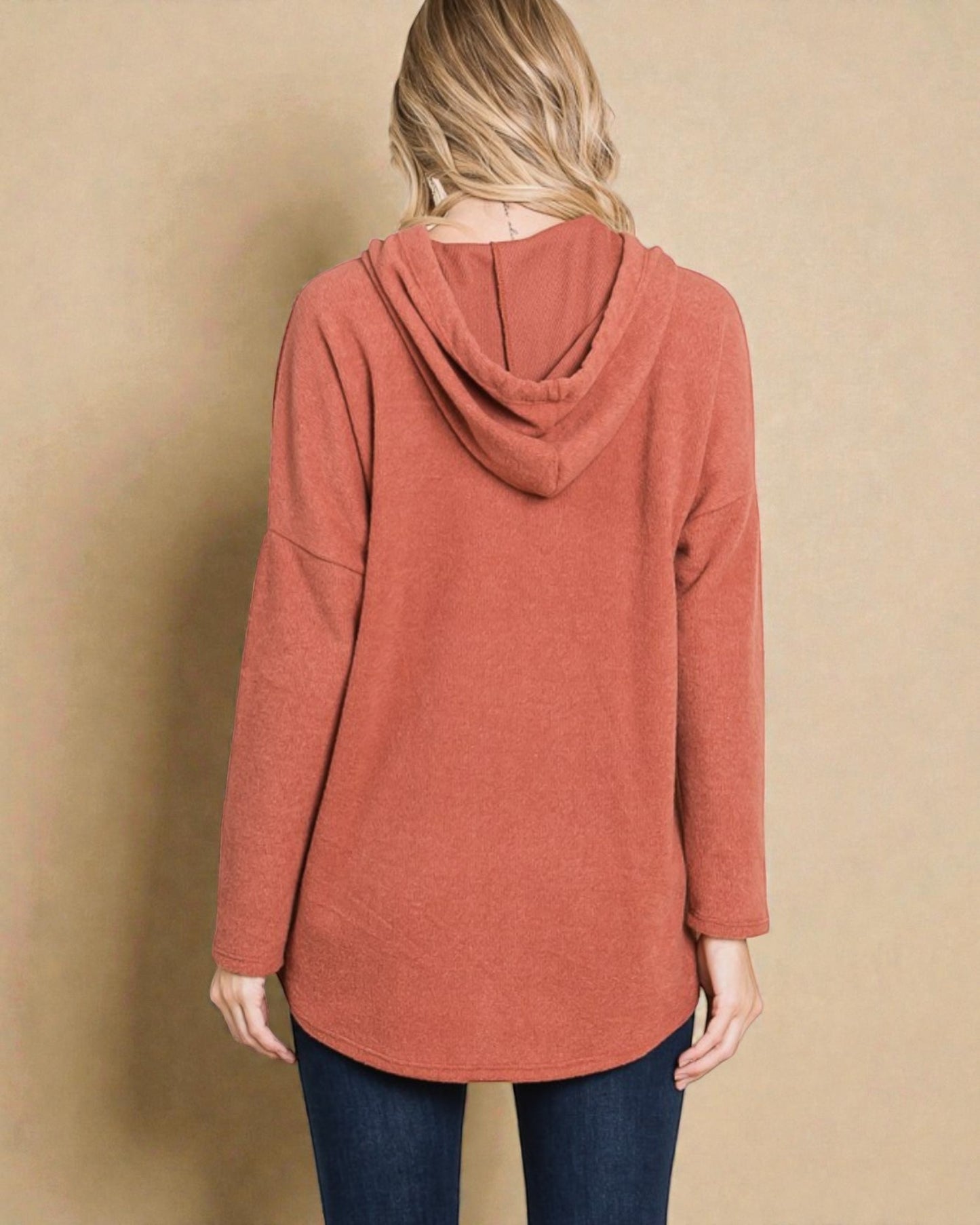 Person wearing a rust-colored hoodie against a beige background