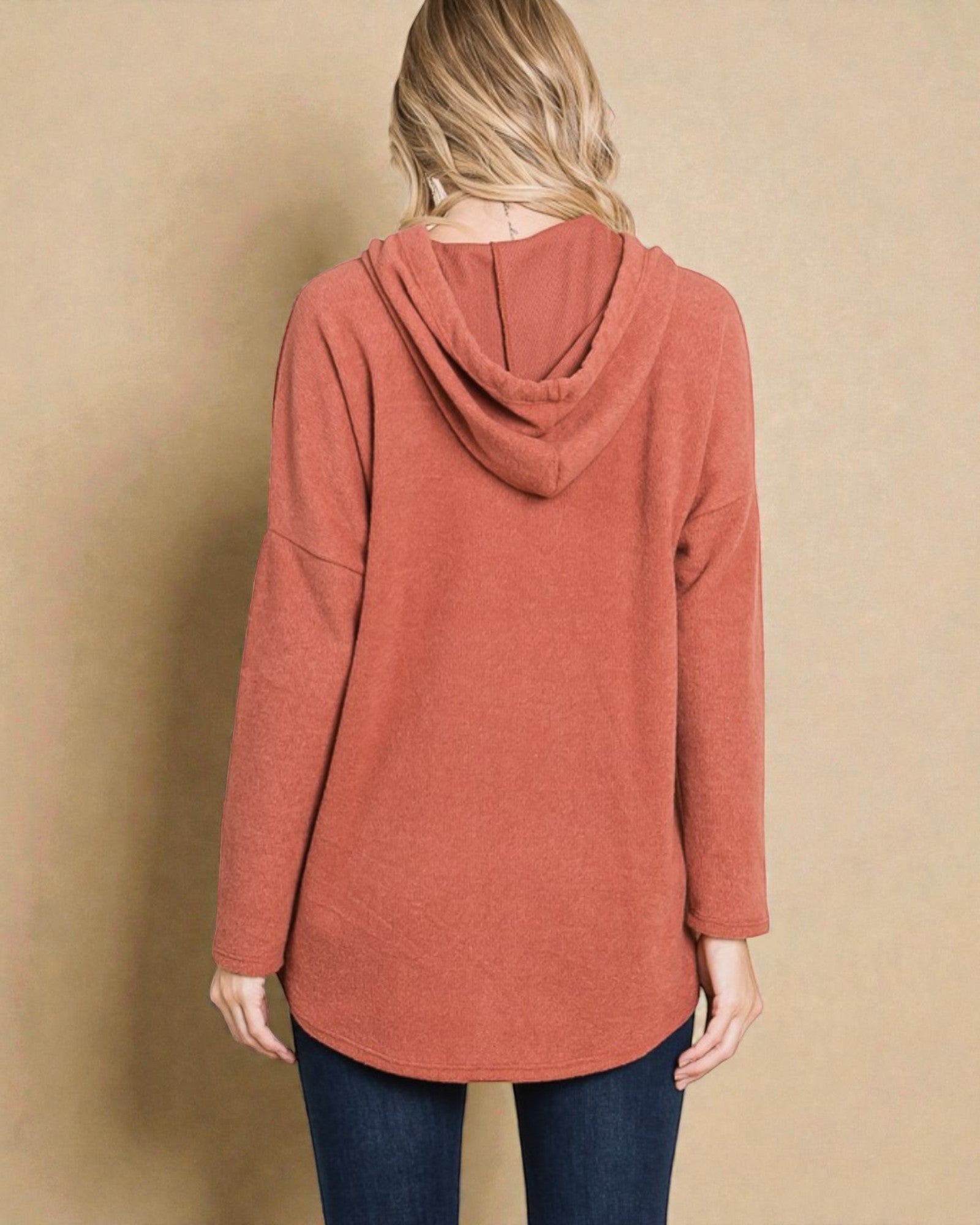 Person wearing a rust-colored hoodie against a beige background