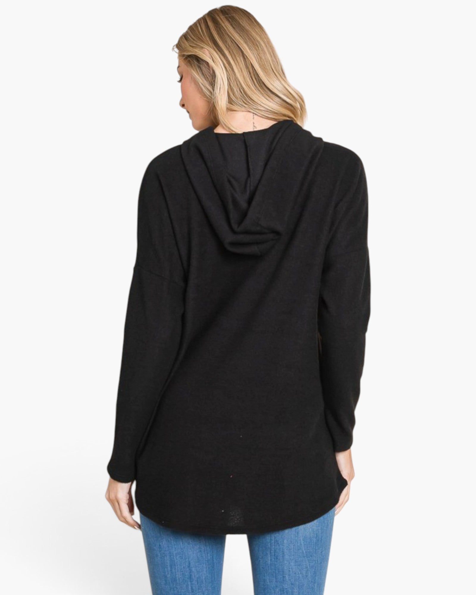 A woman viewed from the back wearing a black long-sleeve hooded tunic top and blue jeans against a plain white studio background.