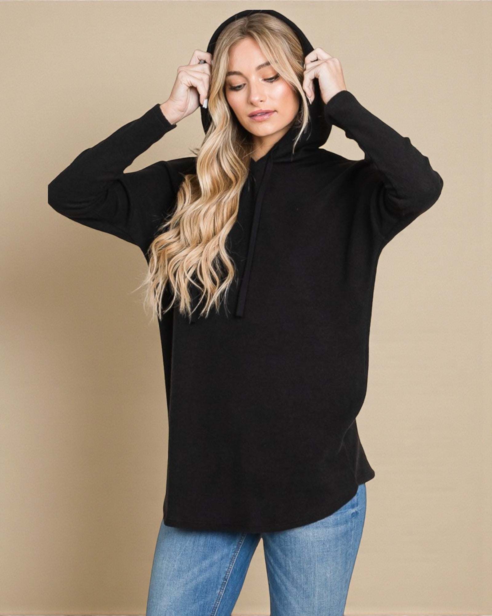 Woman wearing a black hoodie and blue jeans against a beige background