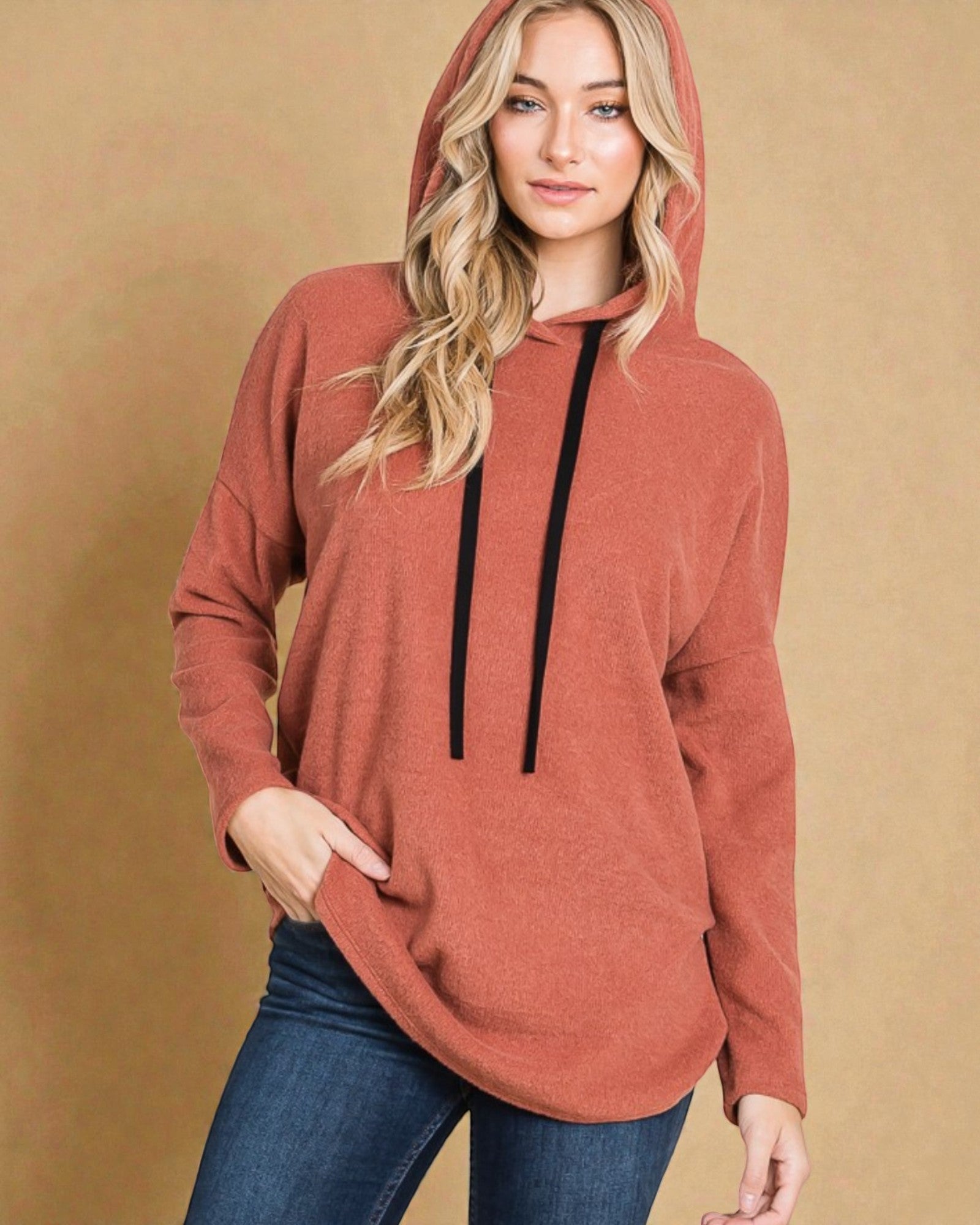 Woman wearing a brown hoodie with a black zipper on a beige background