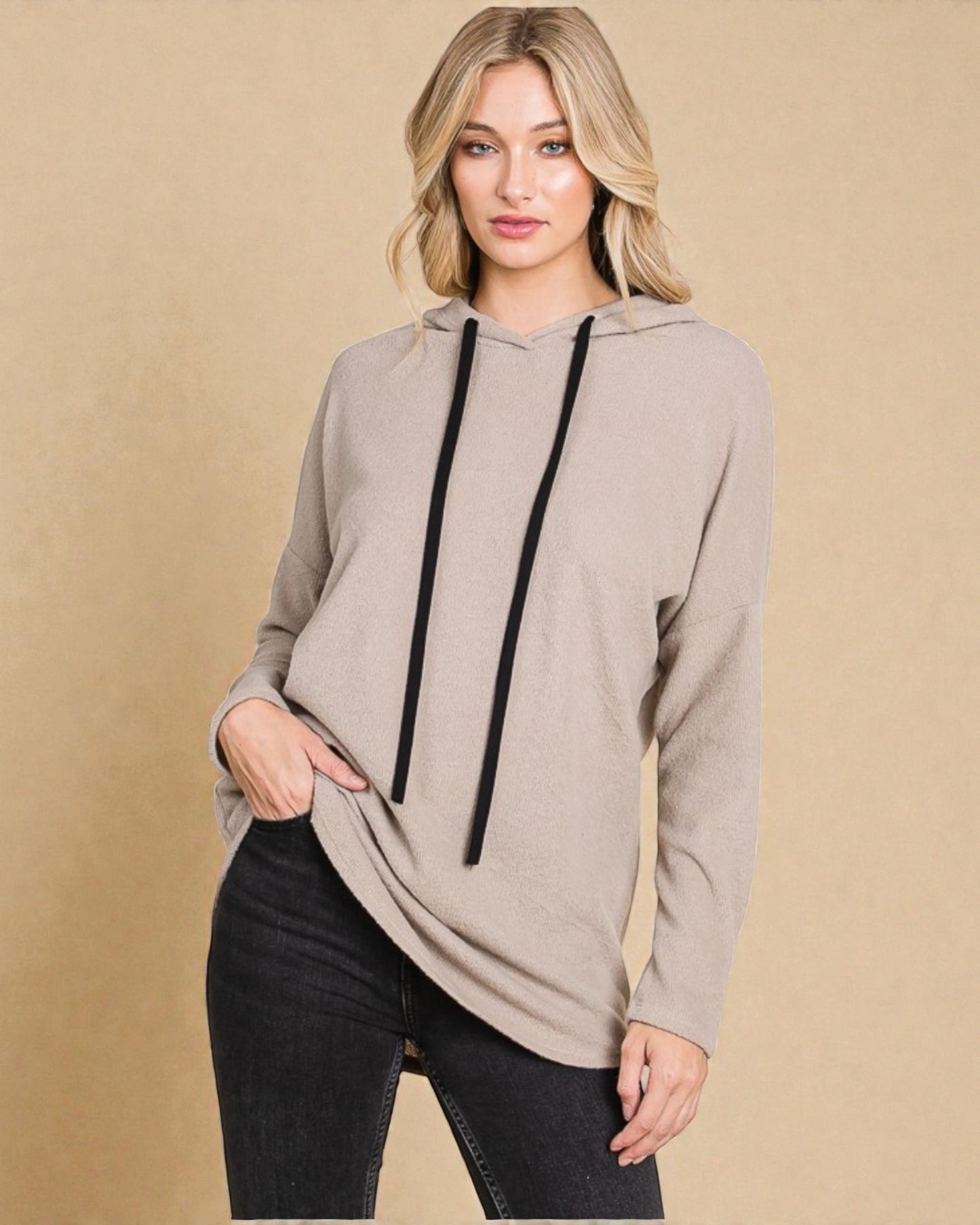 Woman wearing a beige hoodie with black drawstrings on a beige background
