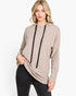 A woman modeling a light taupe-beige long-sleeve hoodie with black drawstrings, paired with black jeans, against a plain white studio background.
