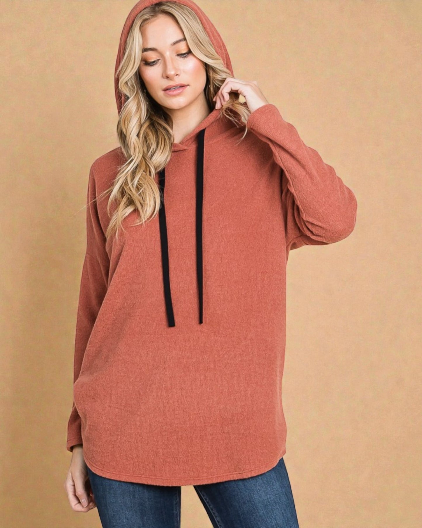 Woman wearing a rust-colored hoodie against a beige background