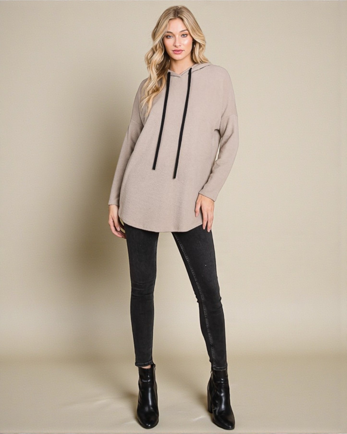 Woman wearing a beige tunic with black accents and black leggings on a beige background