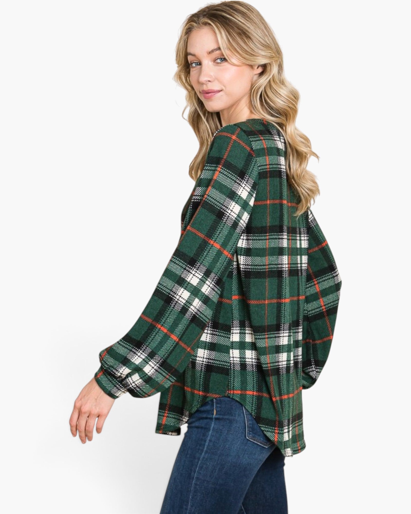 A woman wearing a green plaid long-sleeve top with blue jeans, photographed against a plain light gray studio background.