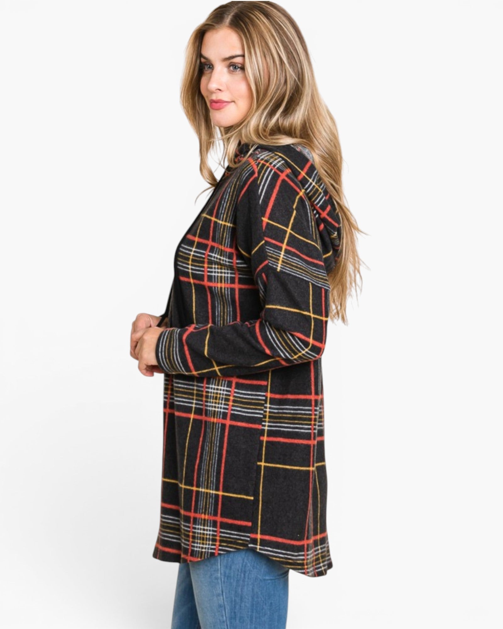 A woman wearing a black long-sleeve plaid tunic top with red, yellow, and white lines, paired with blue jeans, photographed against a plain white studio background.