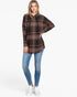 A woman modeling a black long-sleeve plaid top with red, yellow, and white stripes, paired with blue skinny jeans and white sneakers, against a plain white studio background.