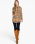 A woman modeling a tan and black plaid hooded sweatshirt with a kangaroo pocket, paired with black leggings and brown knee-high boots, against a plain white background.