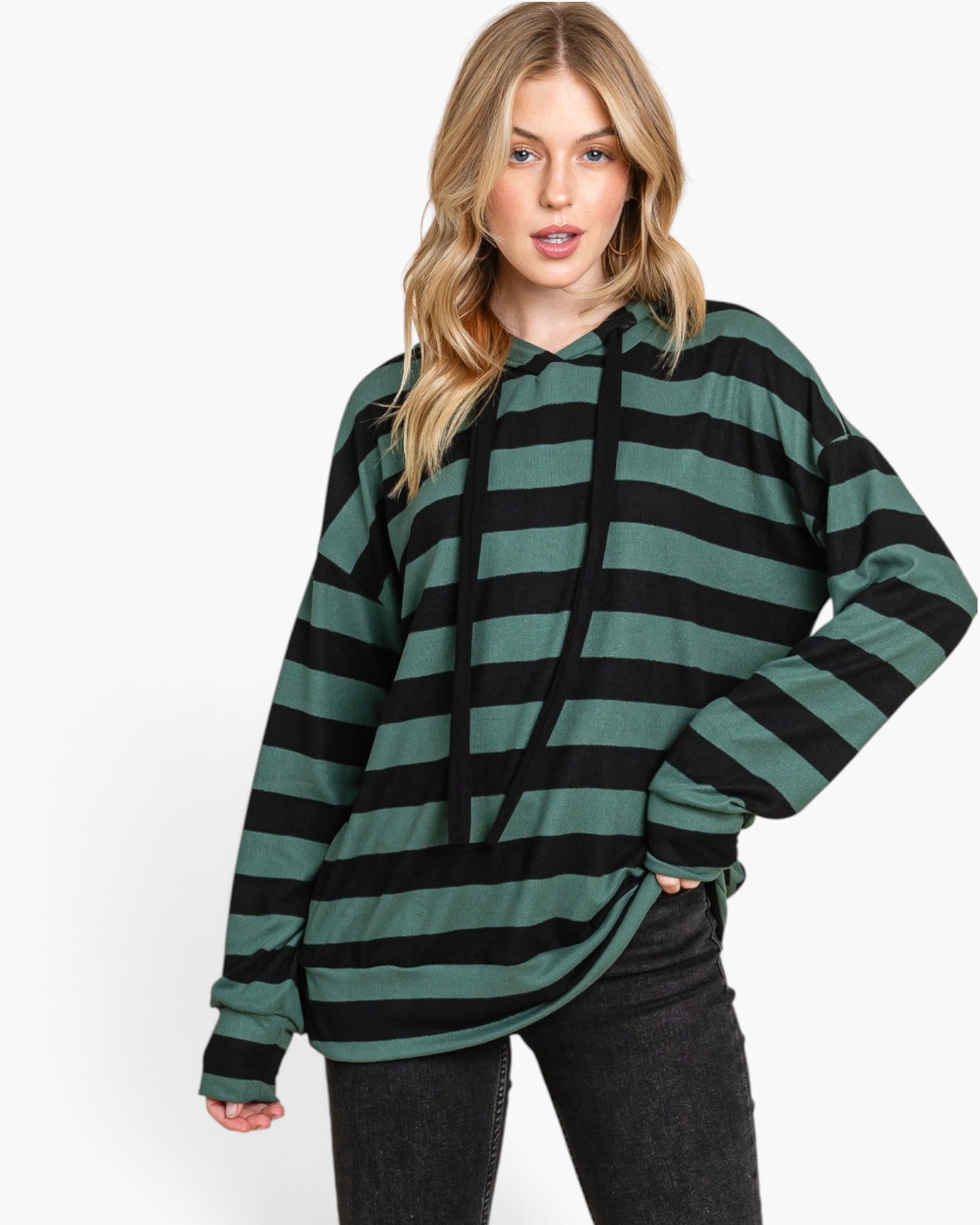 A woman modeling an oversized long-sleeve hoodie with horizontal dark green and black stripes, paired with black jeans, against a plain white studio background.