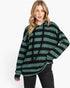 A woman modeling an oversized long-sleeve hoodie with horizontal dark green and black stripes, paired with black jeans, against a plain white studio background.