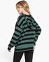 A woman wearing a green and black horizontally striped long-sleeve hoodie, shown from a side-back angle against a plain white studio background.