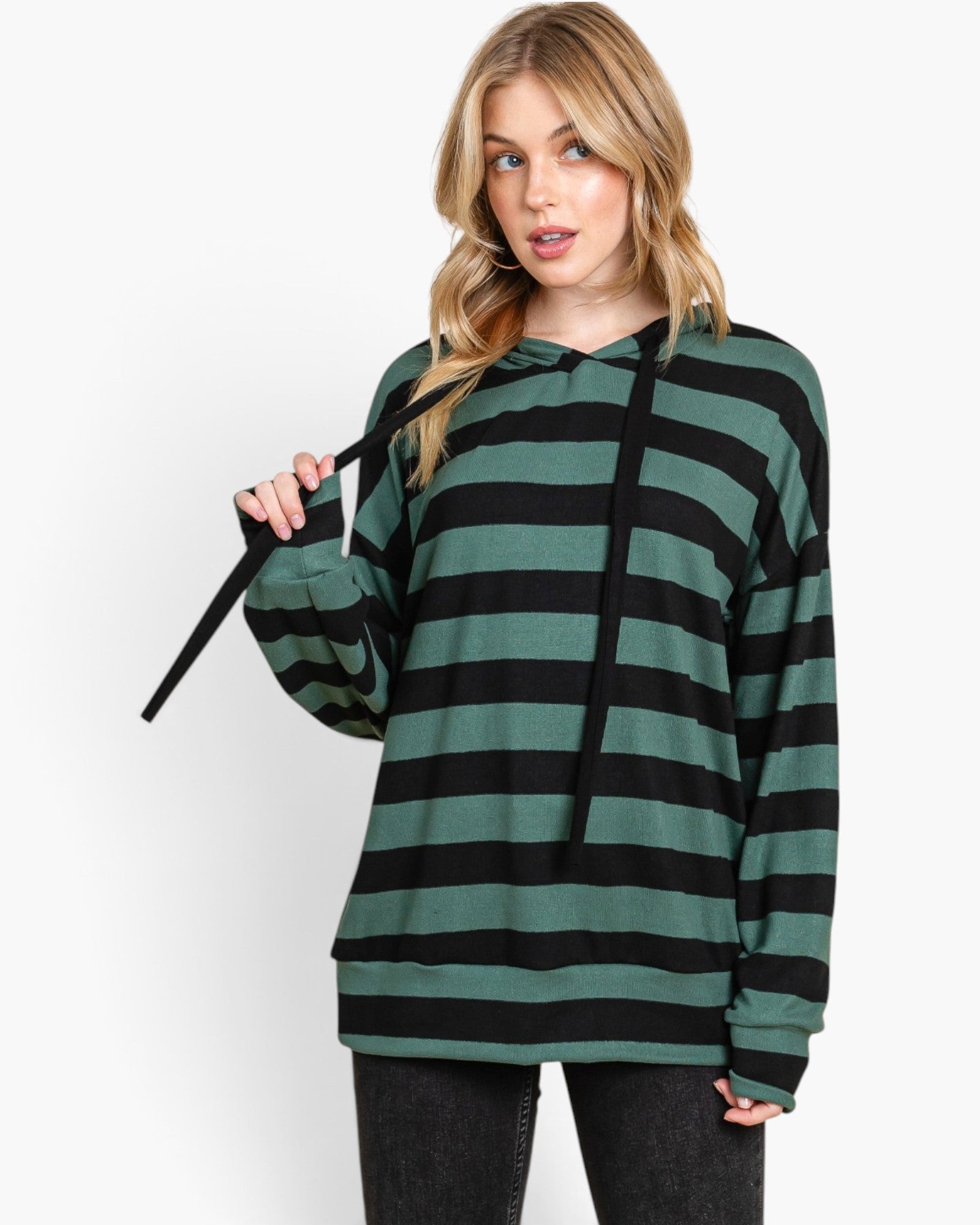 A woman modeling a green and black horizontally striped long-sleeve hoodie with black drawstrings, paired with dark gray jeans, against a plain white studio background.