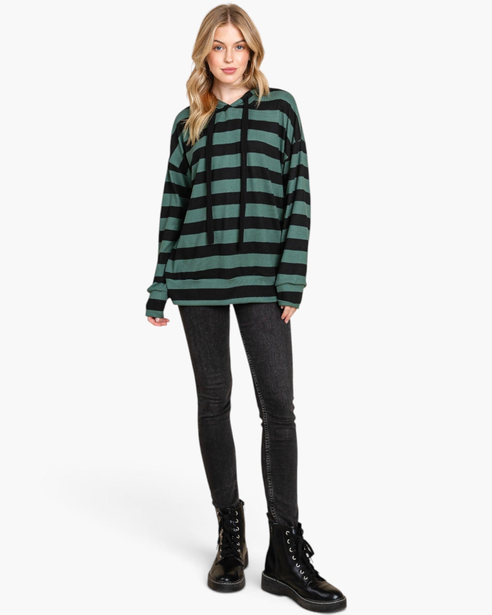 A woman modeling a green and black horizontally striped long-sleeve hoodie, paired with black skinny jeans and black lace-up combat boots, against a plain white studio background.