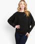 A woman modeling a black long-sleeve knit sweater with a relaxed fit and elbow-length sleeves, paired with dark blue jeans, against a plain white studio background.