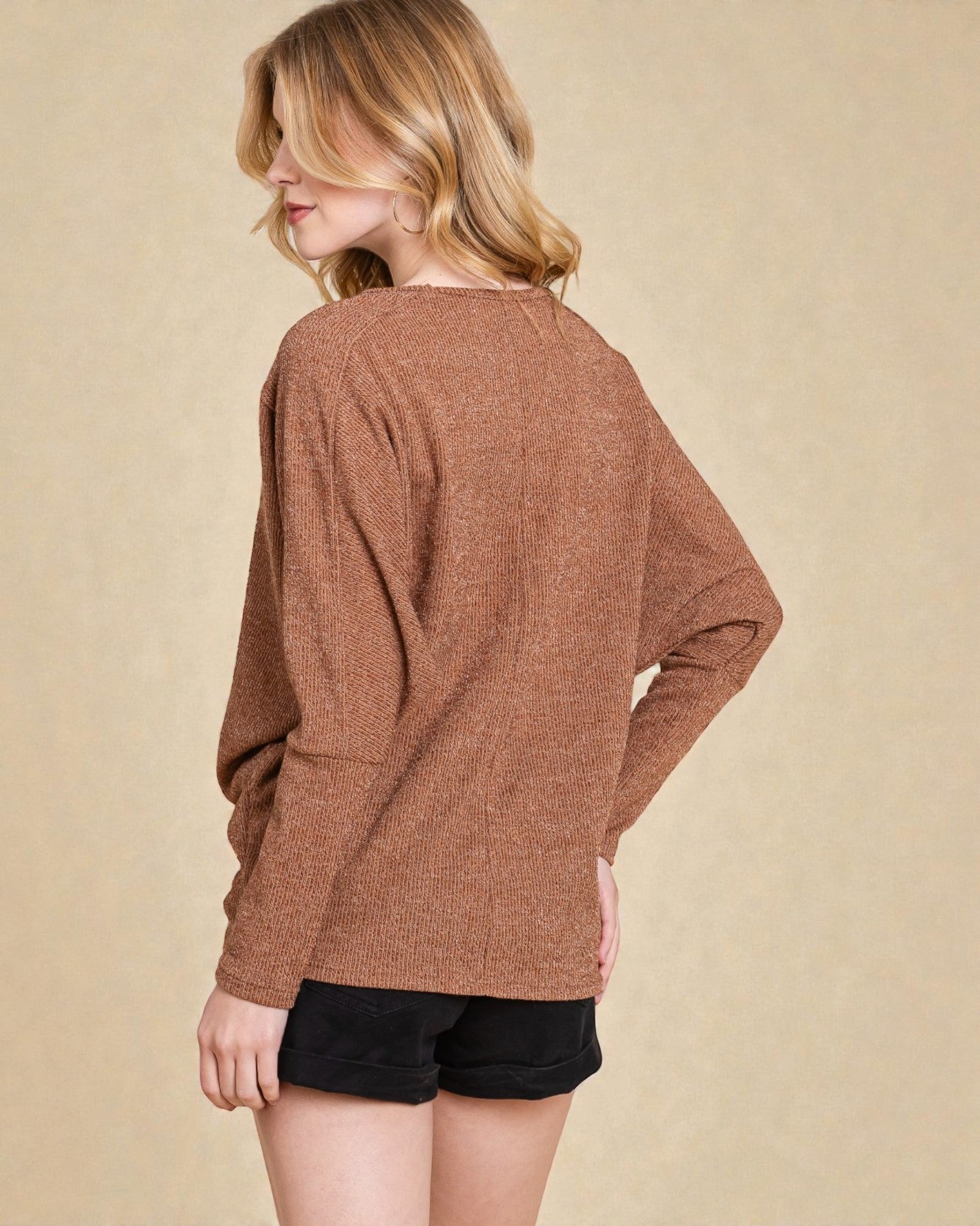 Woman wearing a brown sweater and black shorts on a beige background