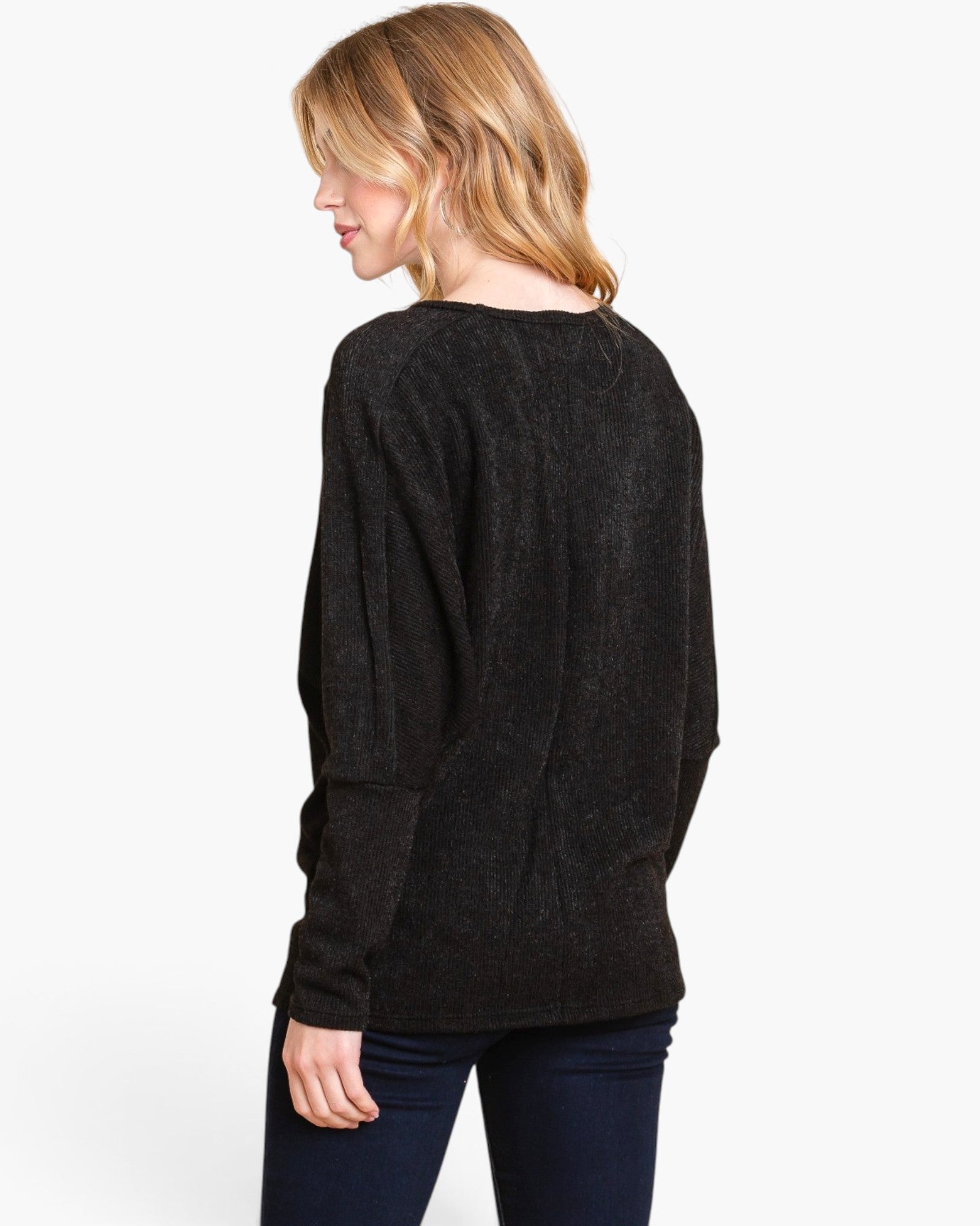 A woman shown from the back wearing a dark charcoal gray knit sweater and dark blue jeans, photographed against a clean white studio background.