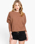 A woman modeling a brown knit sweater with balloon sleeves and black shorts against a plain white background.
