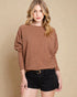 Woman wearing a brown sweater and black shorts against a beige background