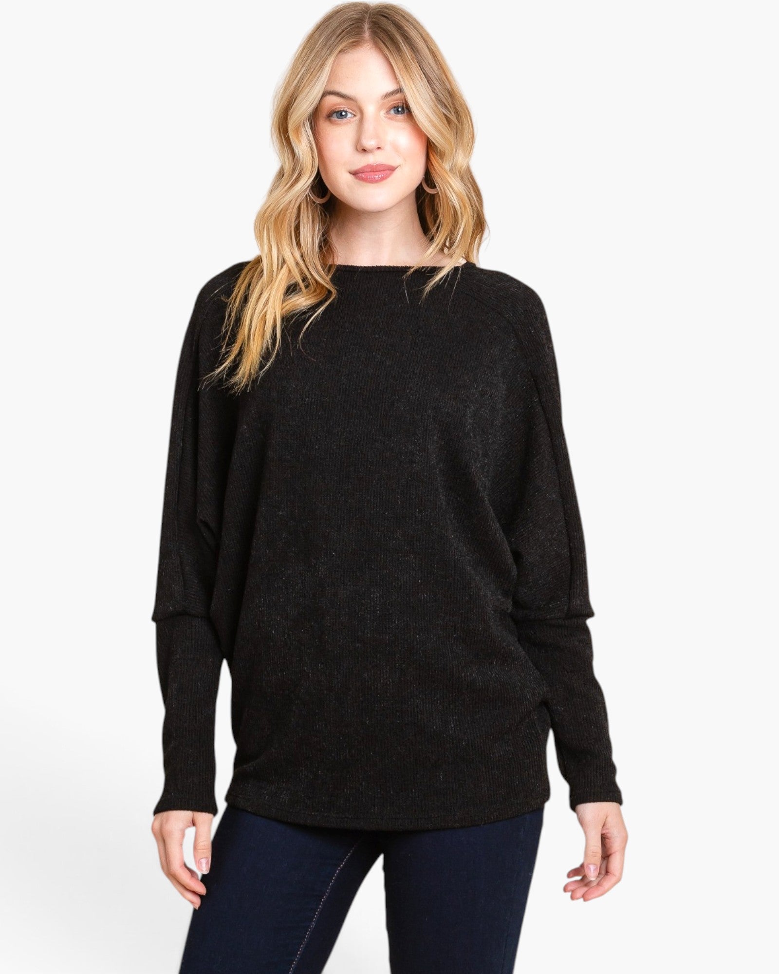 A woman modeling a black long-sleeve knit sweater with a wide boat neckline, photographed against a clean white studio background.