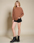 Woman wearing a brown sweater, black shorts, and black boots on a beige background