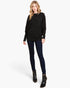 A woman modeling a black long-sleeve knit sweater, dark navy skinny jeans, and black ankle boots against a light gray studio background.