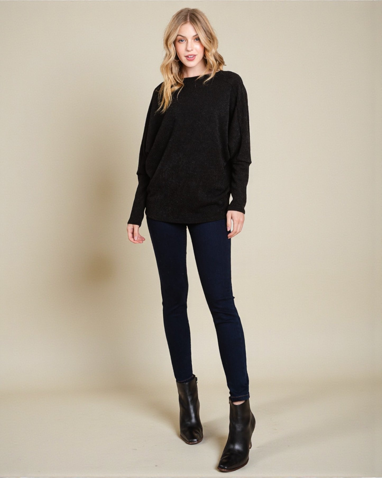 Woman wearing a black sweater, dark jeans, and black boots on a beige background