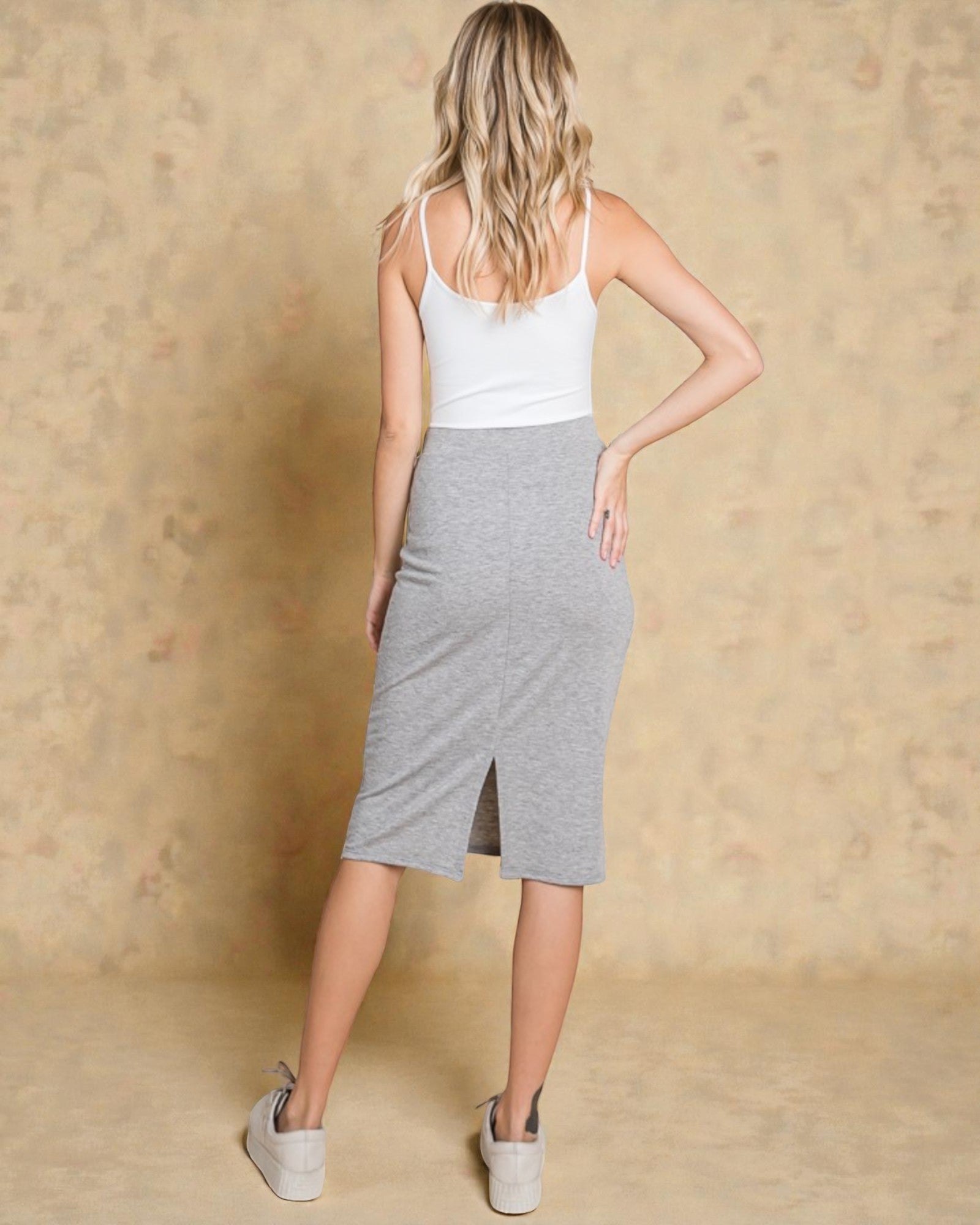 Woman wearing a white tank top and gray skirt against a beige background