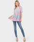 Woman wearing a pink and blue patterned top with blue jeans on a white background