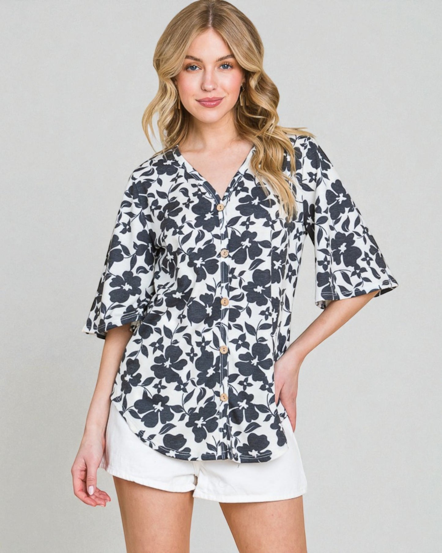 Woman wearing a floral blouse and white shorts on a plain background