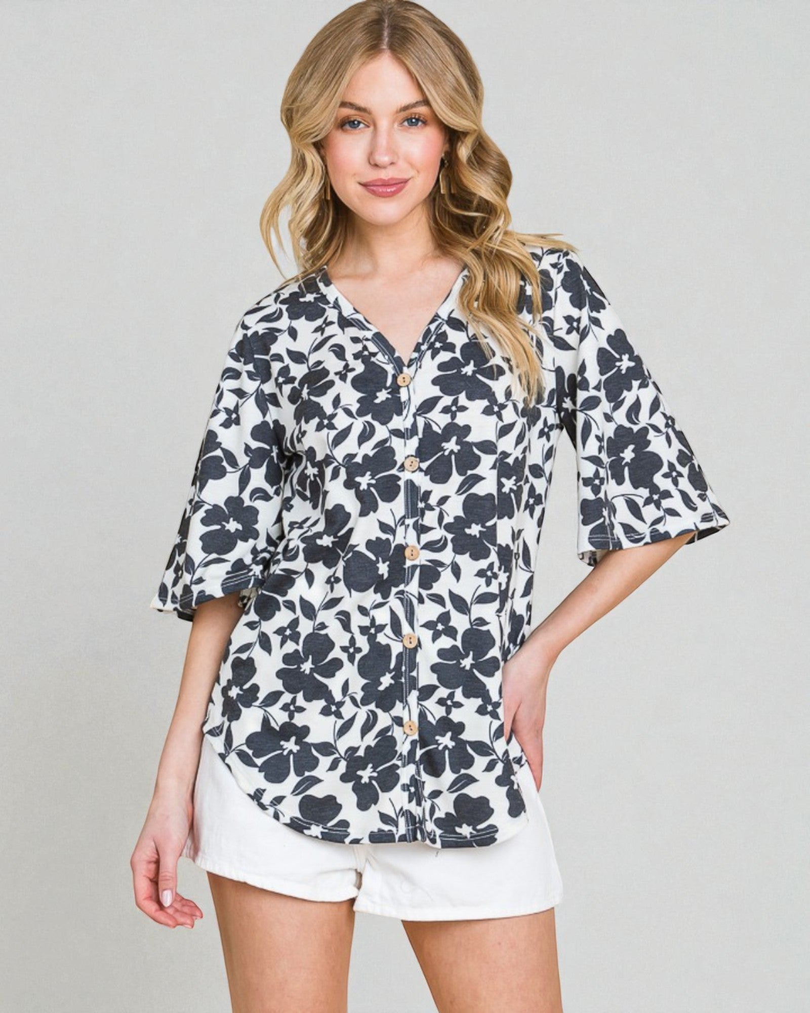 Woman wearing a floral blouse and white shorts on a plain background