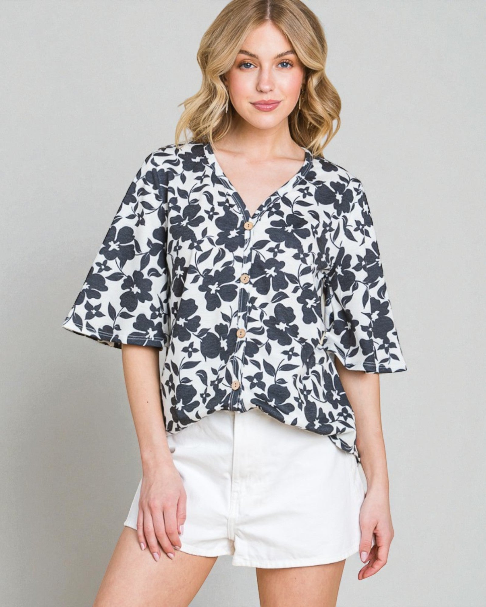 Woman wearing a floral blouse and white shorts on a gray background