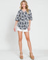 Woman wearing a floral blouse and white shorts on a plain background