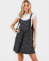 Woman wearing a black floral pinafore dress over a white shirt on a white background