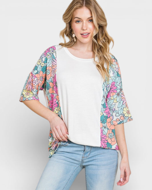 Woman wearing a colorful floral cardigan over a white top and blue jeans on a light gray background