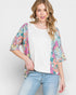 Woman wearing a colorful floral cardigan over a white top and blue jeans on a light gray background