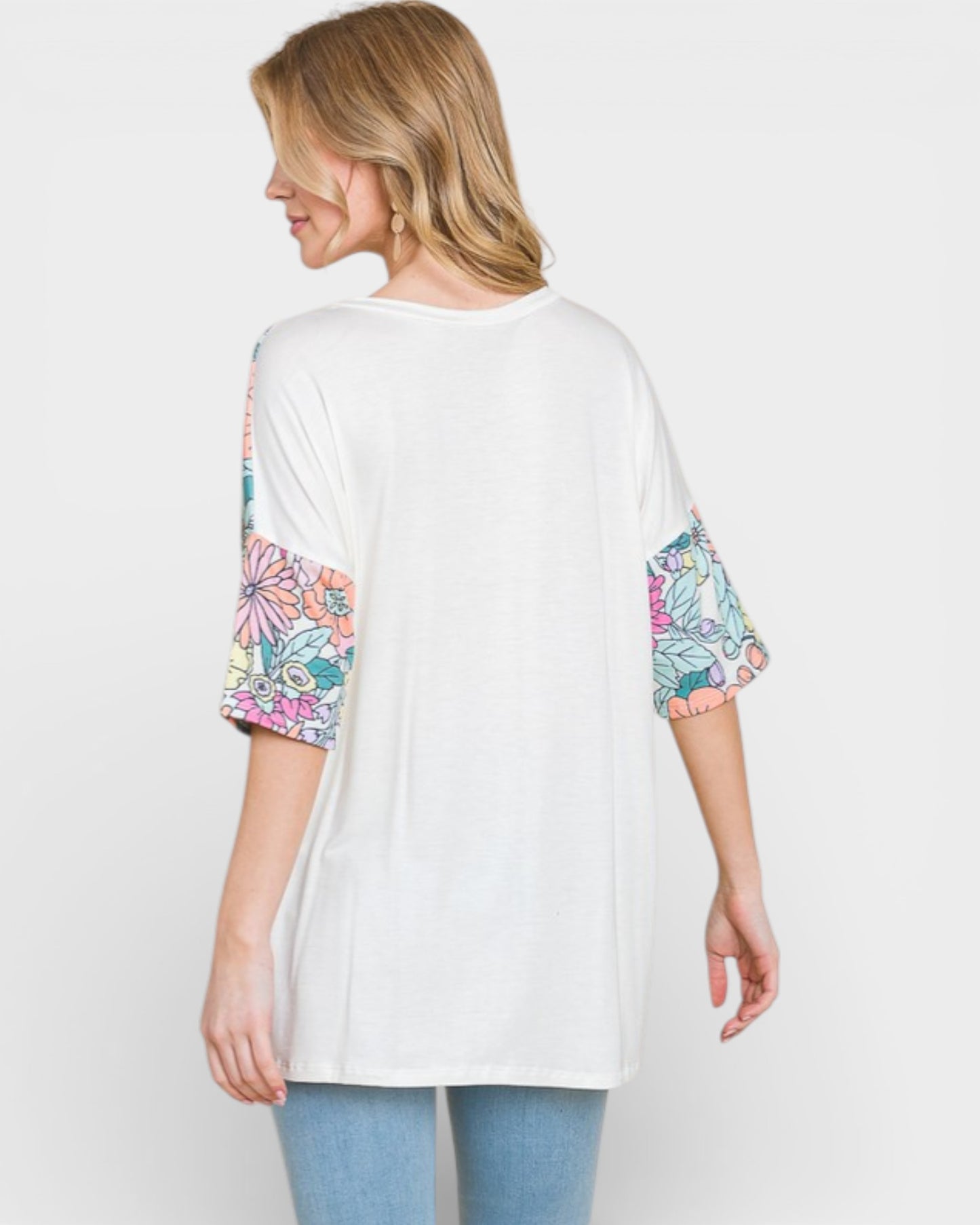 Woman wearing a white tunic with colorful sleeves on a plain background