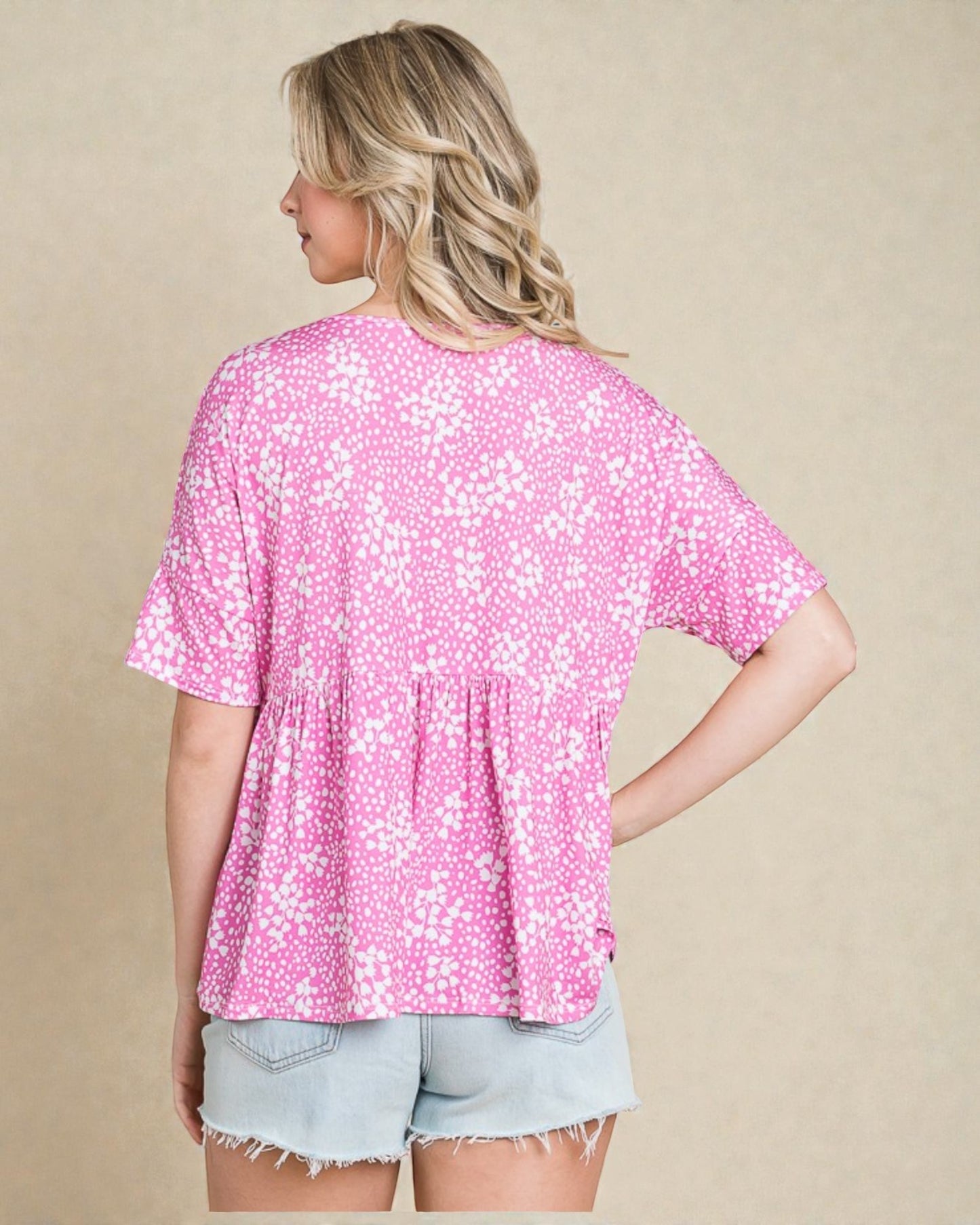 Woman wearing a pink floral blouse and denim shorts on a beige background