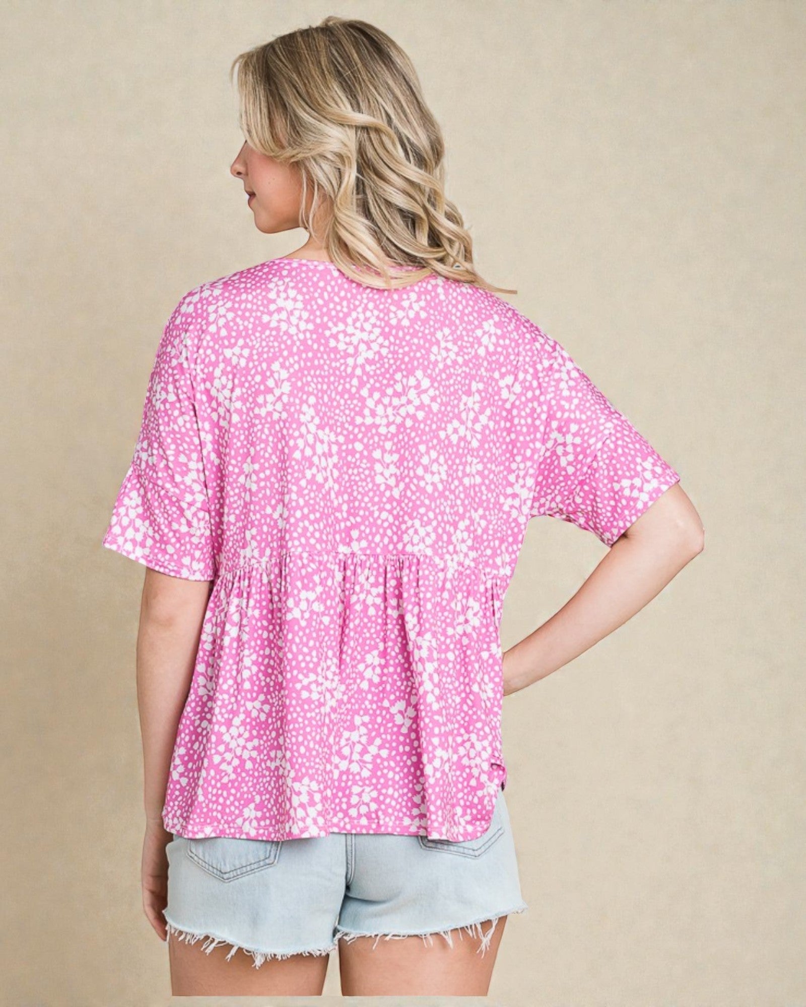 Woman wearing a pink floral blouse and denim shorts on a beige background