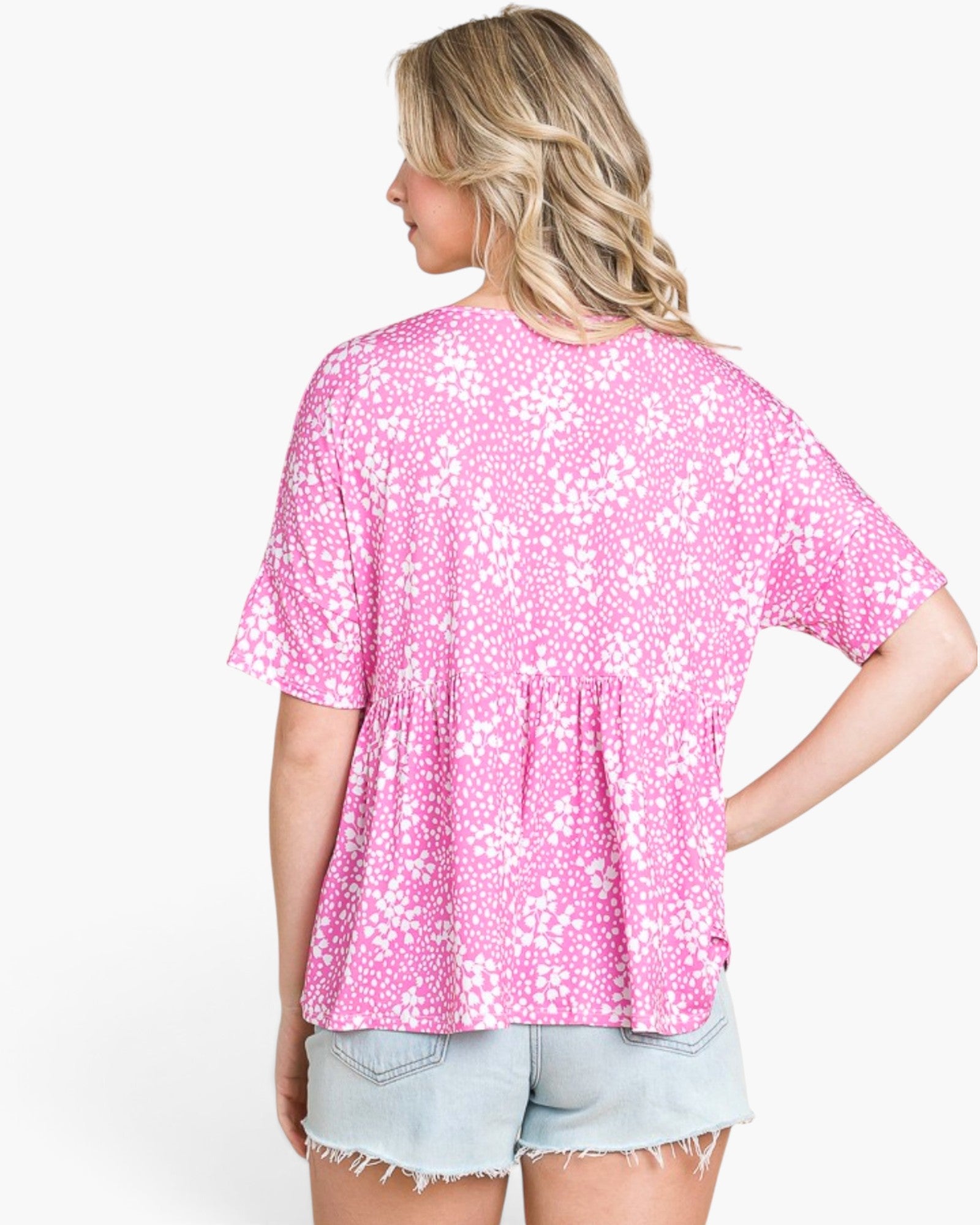 A woman shown from the back wearing a pink short-sleeve top with a white floral pattern and light denim shorts against a plain white background.