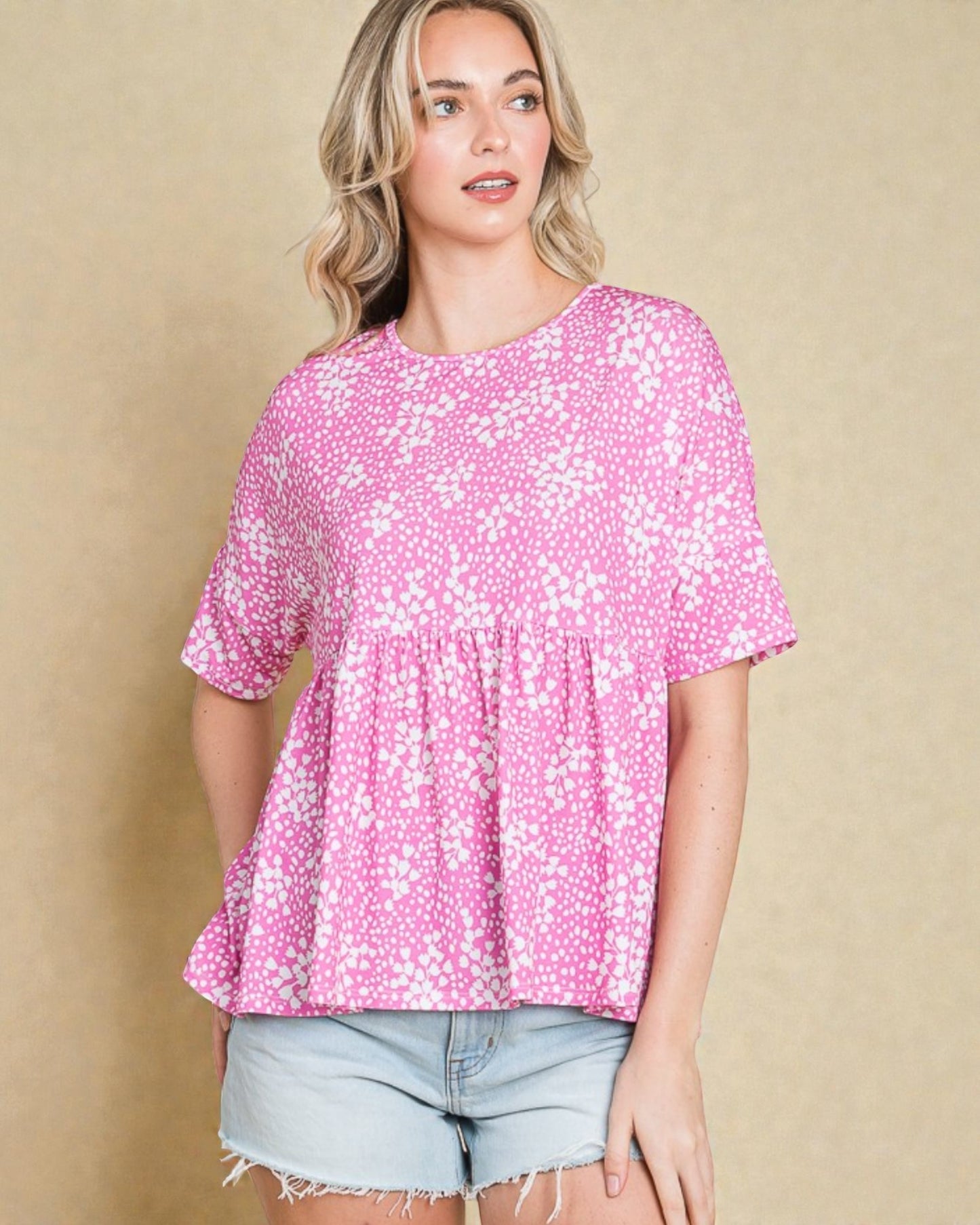 Woman wearing a pink floral blouse and denim shorts against a beige background