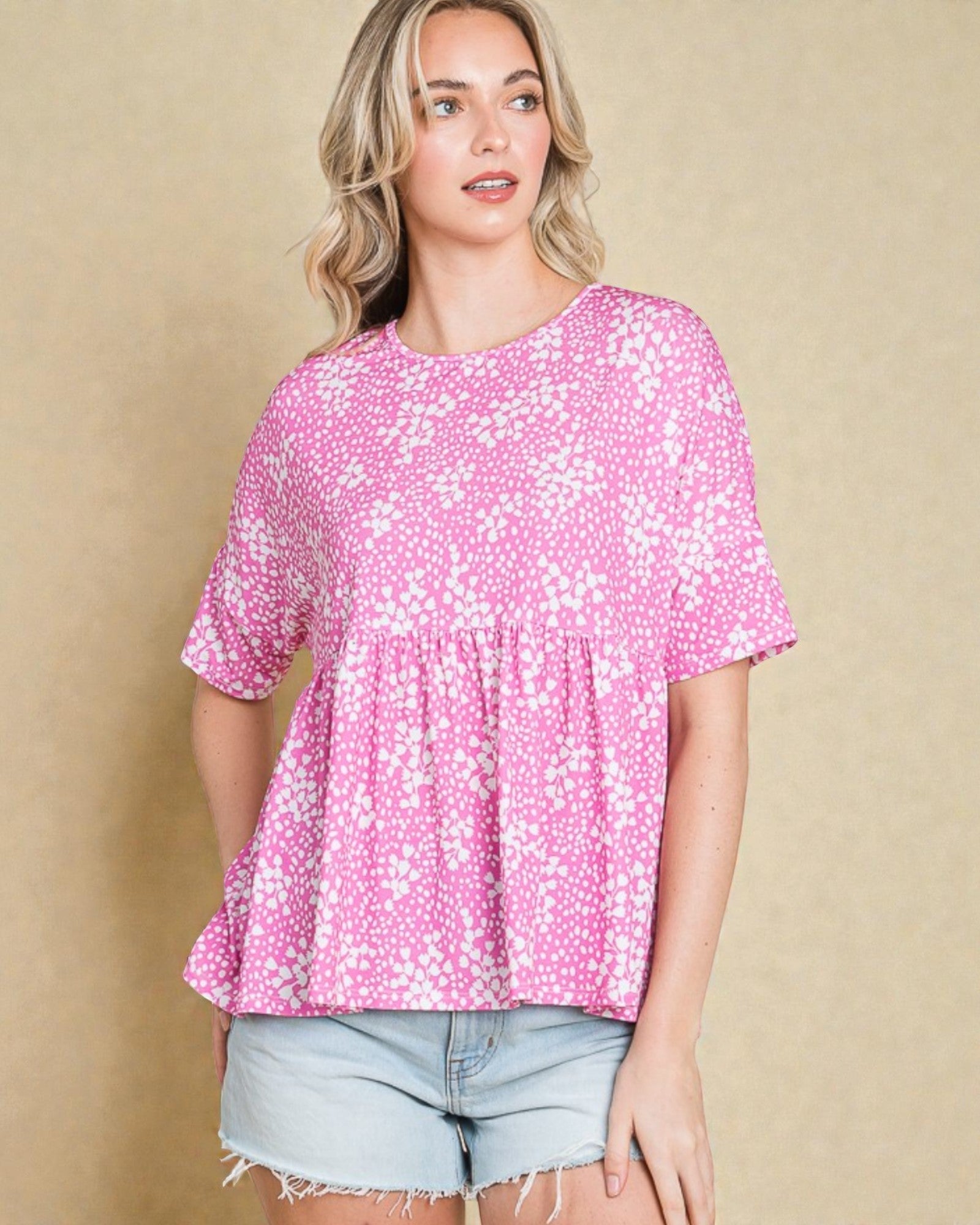 Woman wearing a pink floral blouse and denim shorts against a beige background