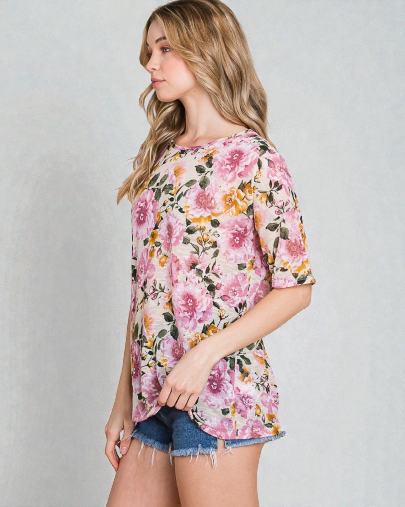 Woman wearing a floral print top and denim shorts on a plain background